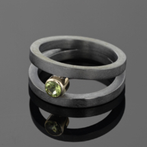 Oxidised silver ring with two bands holding together a Peridot in a ýellow gold setting