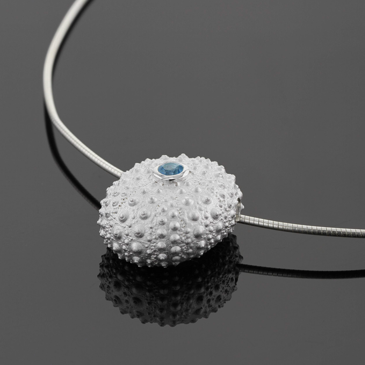 Large, whole sea urchin pendant in sterling silver with a Blue Topas set at its center with a rigid silver chain.