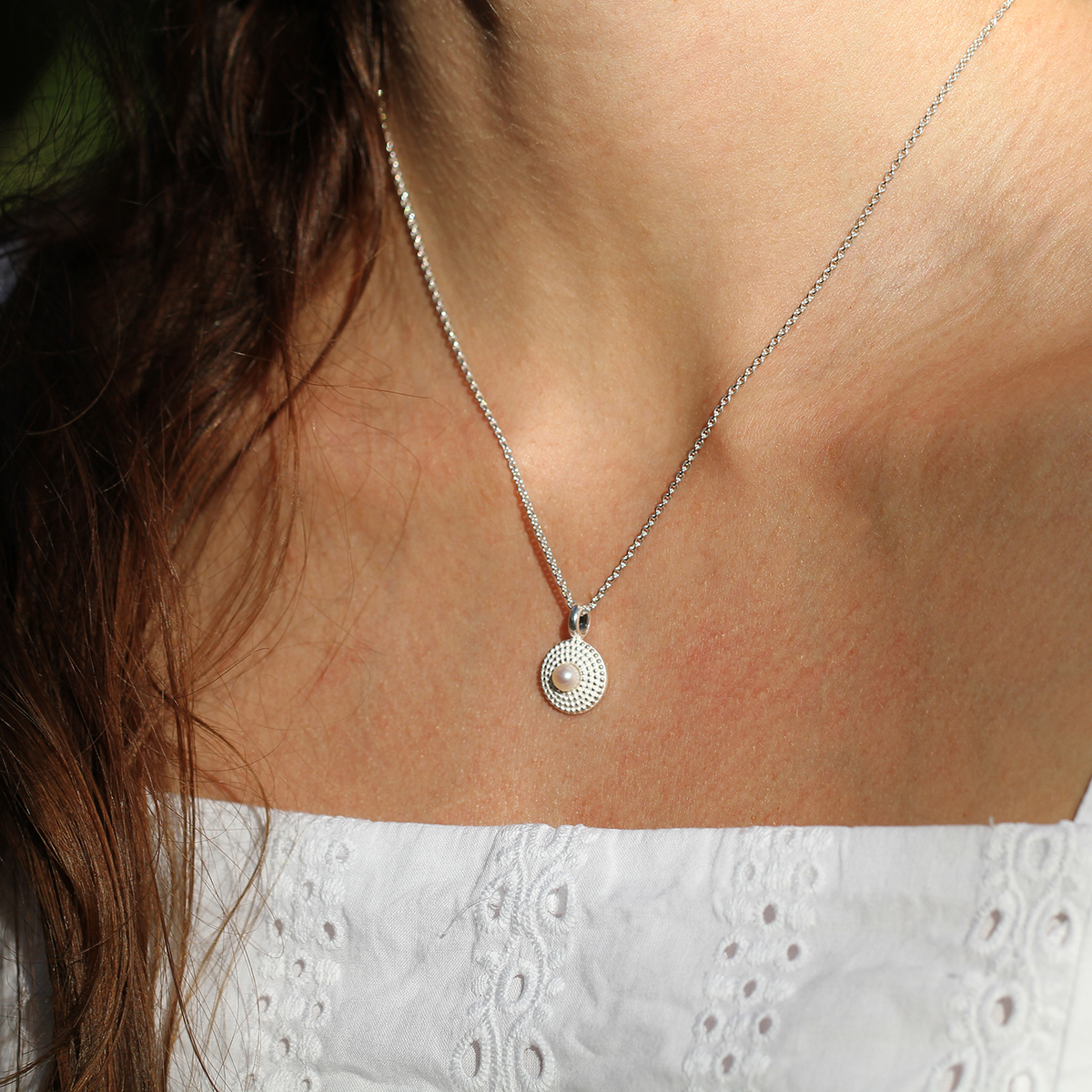 Delicate, circle shaped pendant in sterling silver with a dotted, polished structure and a freshwater pearl sitting at its center.
