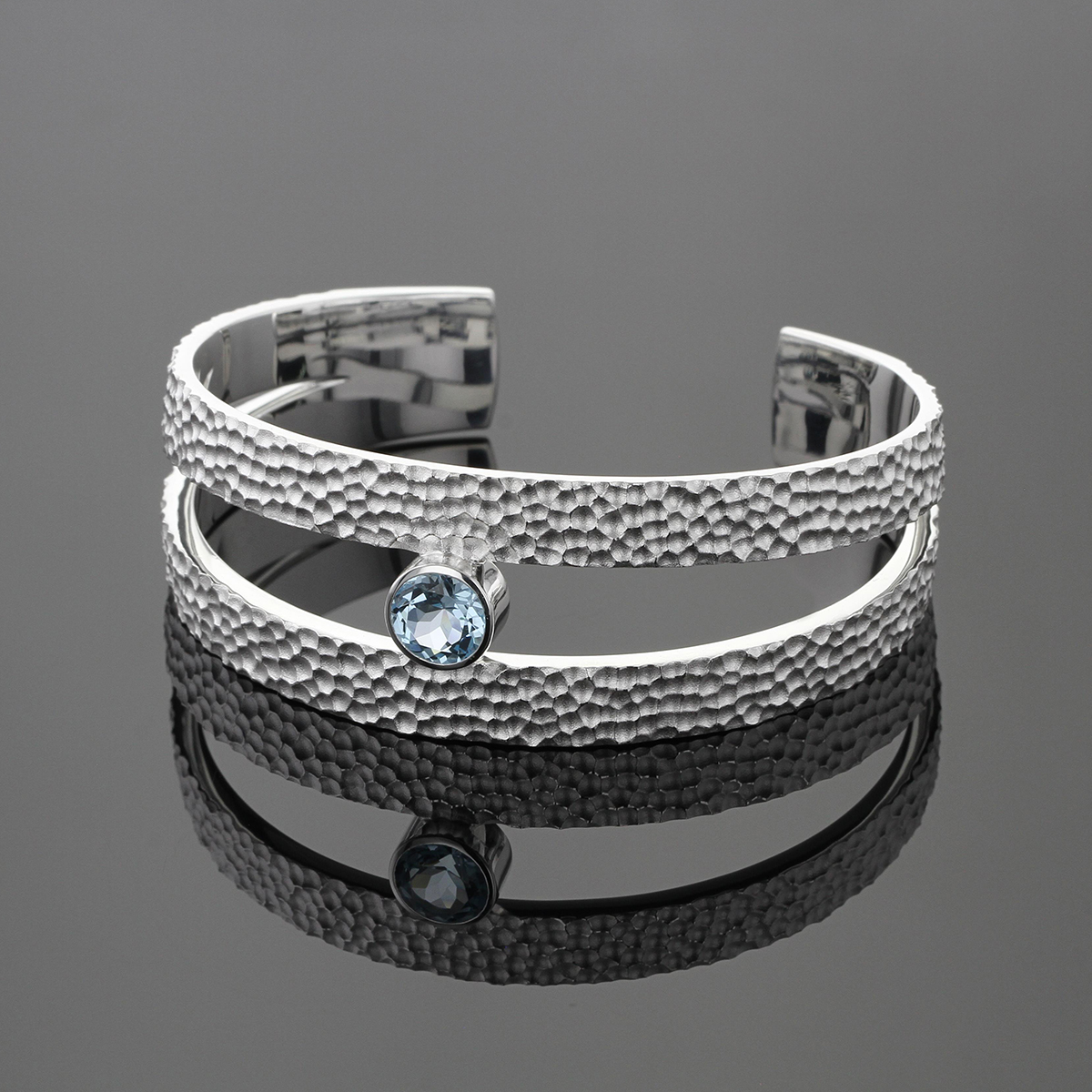 Statement bangle in sterling silver with our unique lava rock texture and a sparkling Blue Topas gem.