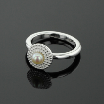 Sterling silver ring with a circular shaped, flat head with a dotted texture and a freshwater pearl sitting at its center.