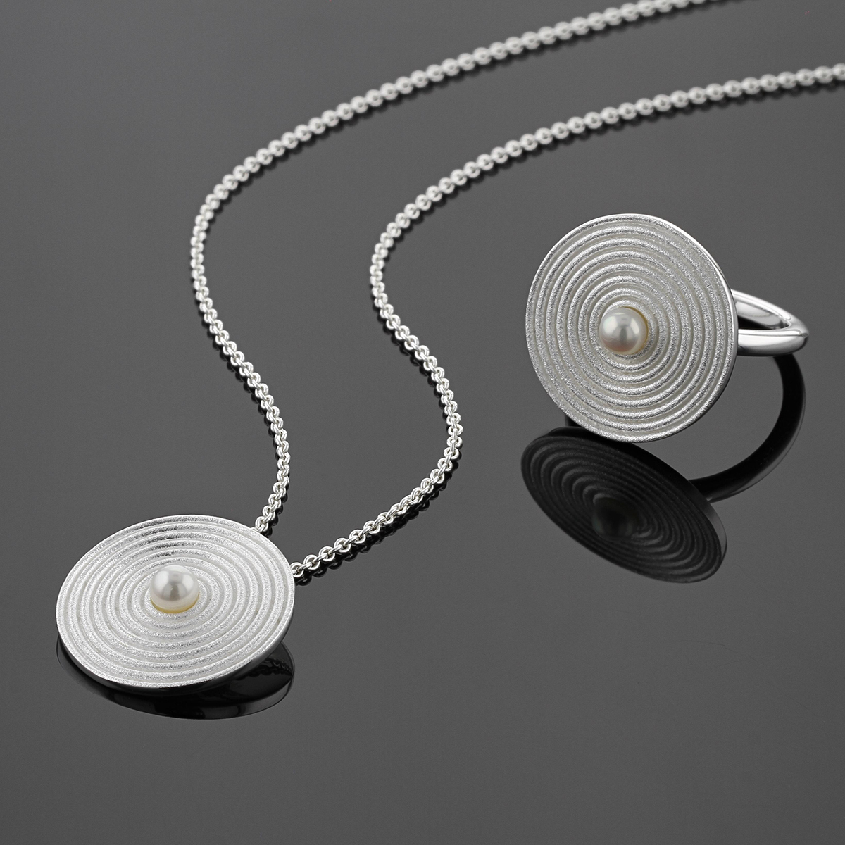 Disc shaped pendant and ring in sterling silver with circular rills originating from freshwater pearls at the center towards the edge.