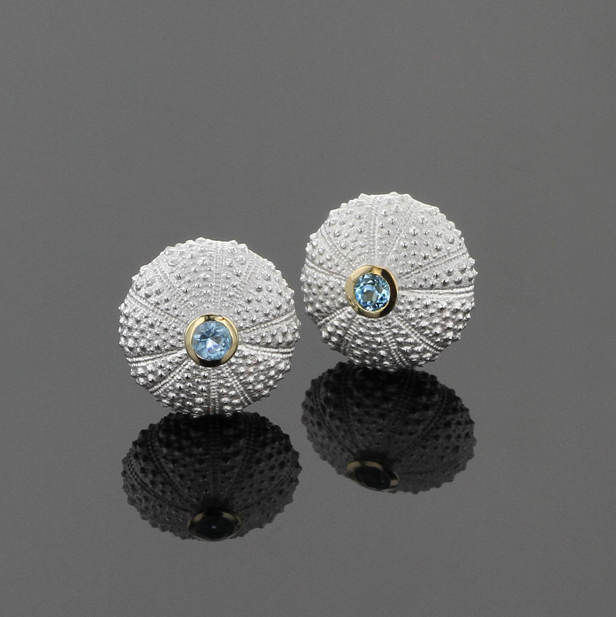 Tiny sea urchin earrings in sterling silver with a Blue Topas stone in a yellow gold setting at its center.