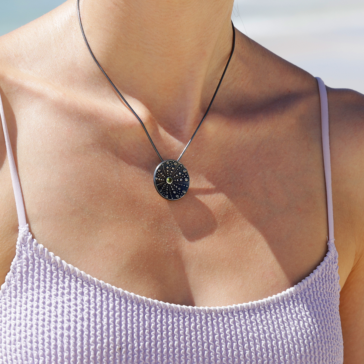 Disc shaped pendant in black silver with sea urchin textures and a Peridot stone