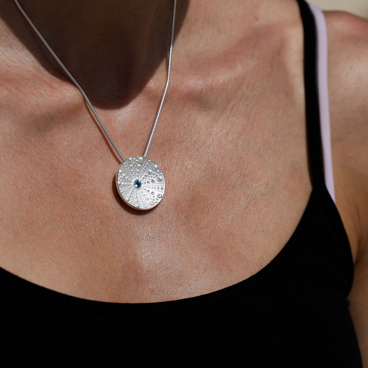 Disc shaped pendant in silver with sea urchin textures and a Blue Topas stone