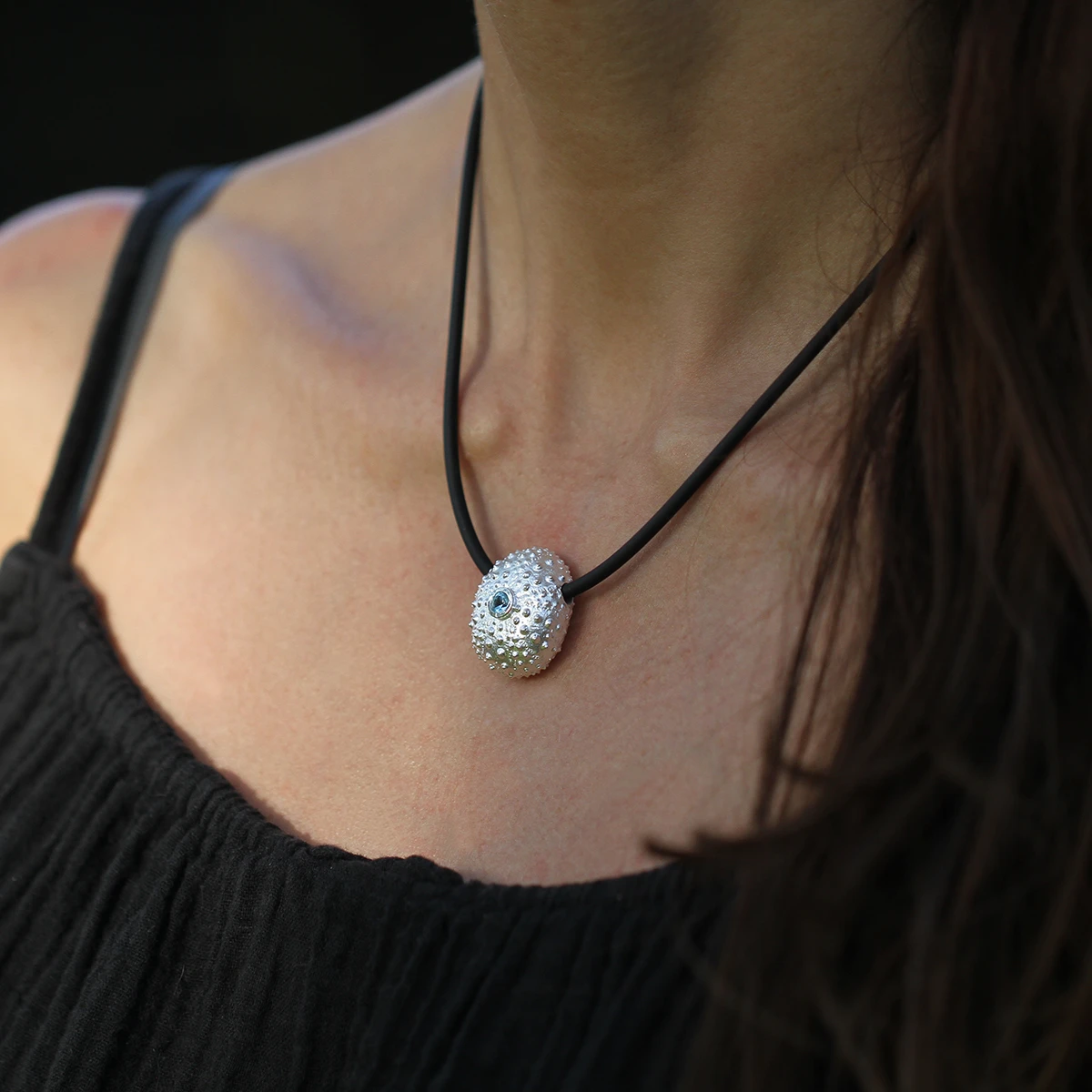 Large, whole sea urchin pendant in sterling silver with a Blue Topas set at its center with a black, rubber chain.