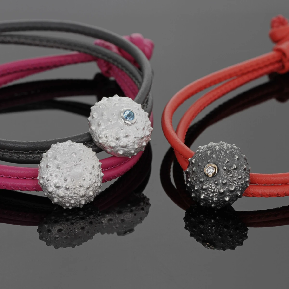 Complete sea urchins in sterling silver on leather bracelets. A black silver and diamond sea urchin on a coral coloured leather, a plain white sea urchin on a hot pink leather and a white sea urchin with Blue Topas stone on a grey leather.